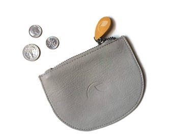 May include: A gray leather coin purse with a zipper closure and a small, light brown leather pull tab. The purse has a crescent moon design embossed on the front.