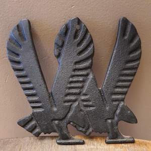 May include: A black cast iron decorative piece in the shape of a bird with outstretched wings. The bird has detailed feather patterns and is designed to stand upright. The piece has a textured surface and a hole at the top for hanging.