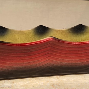 May include: A rectangular ceramic planter with a wavy rim. The planter features a gradient of colors, transitioning from red at the base to black, with a yellow and black interior. The planter is designed with a series of horizontal ridges.