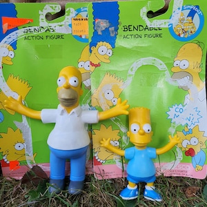 May include: Two bendable Simpsons action figures, Homer and Bart, are displayed in their original packaging. Homer wears a white shirt and blue pants, while Bart sports a blue shirt and shorts. The packaging features images of the Simpsons family and the text "BENDABLE ACTION FIGURE."