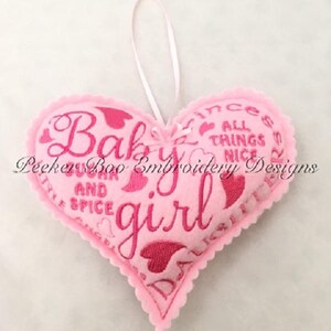 May include: Pink felt heart-shaped ornament with pink embroidery that reads "Baby girl" and other phrases including "sugar and spice" and "all things nice".