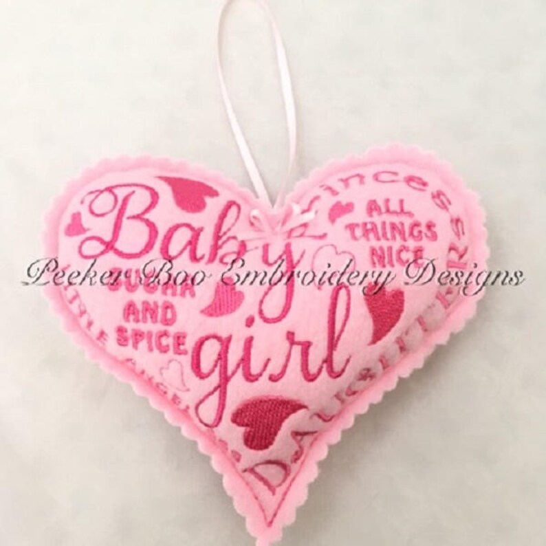 May include: Pink felt heart-shaped ornament with pink embroidery that reads "Baby girl" and other phrases including "sugar and spice" and "all things nice".