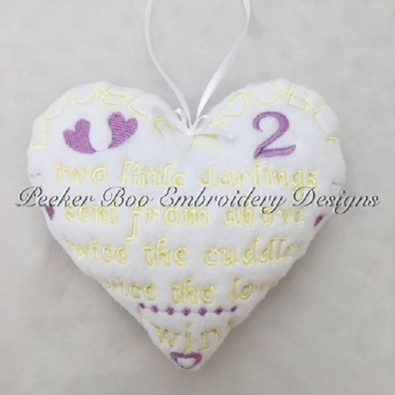 May include: White heart-shaped pillow with yellow and purple embroidery. The pillow reads "Two little darlings sent from above twice the cuddles twice the love twins".
