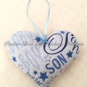 May include: A gray heart-shaped pillow with blue embroidery that reads "Baby Boy" and "Little Son" with stars. The pillow has a blue ribbon attached for hanging.