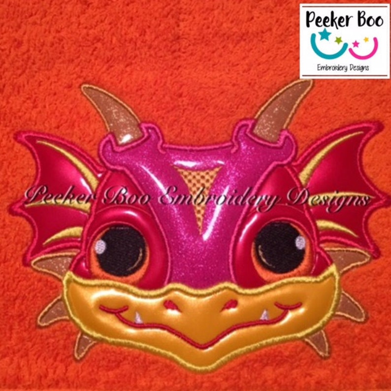 May include: Embroidered design of a red and gold dragon head with large eyes. The dragon has a toothy grin and is looking directly at the viewer. The design is perfect for adding a whimsical touch to any project.