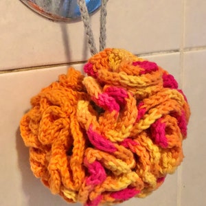 Può includere: Un pouf da bagno all'uncinetto arancione, giallo e rosa appeso a un gancio in un bagno.