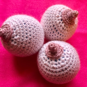 May include: Three crocheted balls with pink crocheted accents. The balls are white with a light blue hue.