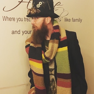 Può includere: Una persona che indossa un cappello nero con occhiali steampunk e una sciarpa a righe multicolori. Il cappello ha ingranaggi e chiavi attaccati. La persona indossa una giacca nera e una camicia bianca. Lo sfondo è un muro bianco con testo marrone che dice "Where you treat and your like family".