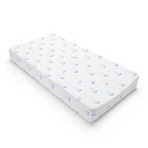 May include: White changing pad cover with a repeating pattern of blue sailboats. The cover is rectangular and has rounded corners. The sailboats are simple line drawings, creating a nautical theme.
