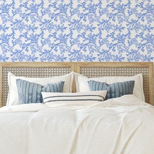 Pode incluir: Um quarto com uma cama branca com almofadas de padr&atilde;o azul e branco e uma cabeceira branca. As paredes s&atilde;o cobertas com um papel de parede floral azul e branco. H&aacute; duas mesas de cabeceira com l&acirc;mpadas e cestos de cada lado da cama.