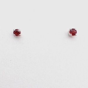 May include: A pair of silver stud earrings with small, oval-shaped red gemstones.