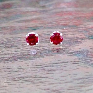 May include: A pair of silver stud earrings with small, round, red gemstones.