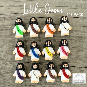 May include: A collection of twelve small figurines of Jesus, each wearing a white robe and a colored sash printed with the text Jesus loves you. The sashes appear in green, brown, orange, white, red, blue, yellow, pink, purple, and tan colors.