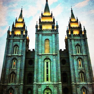 May include: A large, gray stone building with three towers and a golden statue on top. The building has many windows and is lit up at night. The sky is a light blue with clouds.