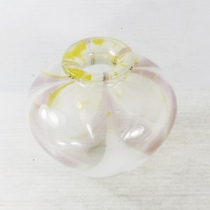 May include: A clear glass vase with a round body and a circular opening. The vase has a white base with pink and yellow swirls throughout. The vase is likely used for decorative purposes.