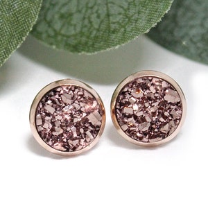 May include: A pair of rose gold stud earrings with a glittery, textured finish.