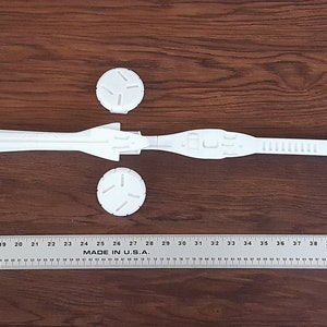 Puede incluir: Un modelo de nave espacial de pl&aacute;stico blanco, desmontado en varias piezas. Las piezas incluyen el cuerpo principal, dos alas, un cono de nariz y una peque&ntilde;a pieza cil&iacute;ndrica. El modelo est&aacute; dispuesto sobre una superficie de madera.