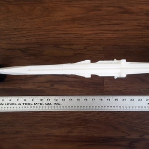 Puede incluir: Modelo de ca&ntilde;&oacute;n blanco de pl&aacute;stico sobre ruedas, que mide aproximadamente 69 cm de largo. El ca&ntilde;&oacute;n est&aacute; sobre una superficie de madera.