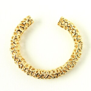 May include: A gold-toned bangle bracelet with a delicate, intricate design that resembles coral. The bracelet is open and has a circular shape.
