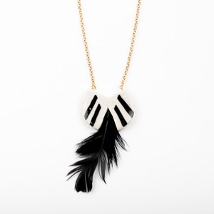 May include: A black and white ceramic necklace with a feather pendant. The necklace has a gold chain and the pendant is shaped like a heart with black stripes.