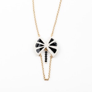 May include: A gold chain necklace with a black and white ceramic pendant shaped like a butterfly. The pendant has a black bead drop.