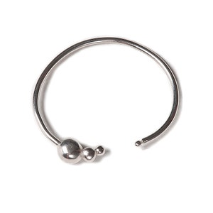May include: A silver bangle bracelet with a cluster of three round beads at the opening.