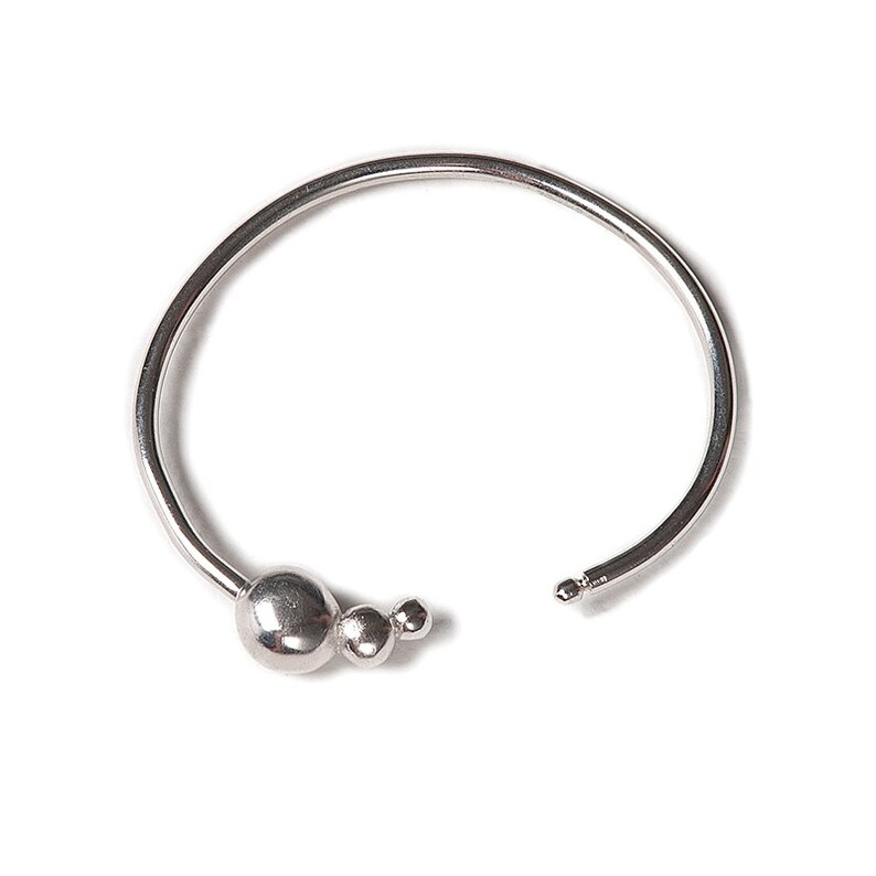 May include: A silver bangle bracelet with a cluster of three round beads at the opening.