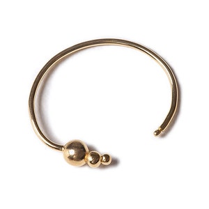 May include: A gold-toned bangle bracelet with a cluster of three round beads on one side.