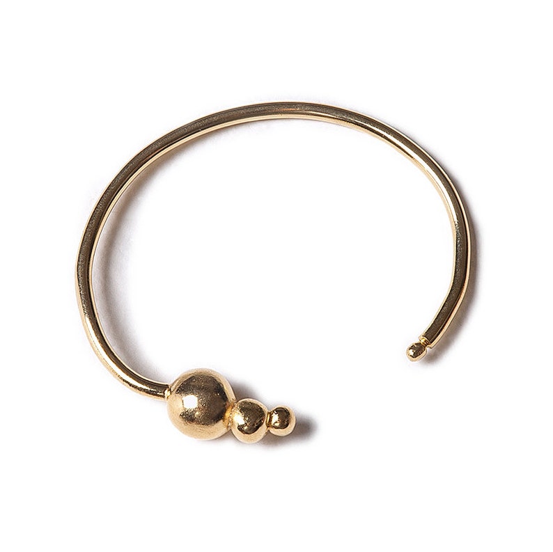 May include: A gold-toned bangle bracelet with a cluster of three round beads on one side.