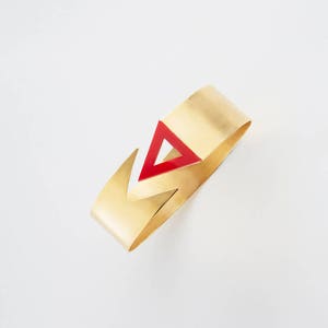 May include: A gold metal bracelet with a red triangle design.