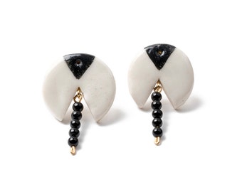 May include: A pair of white ceramic earrings with black geometric designs and black bead dangles.