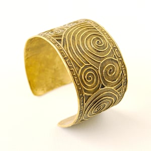 May include: A gold-toned metal cuff bracelet with a decorative design of concentric circles and spirals.
