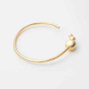 May include: A gold bangle bracelet with a cluster of three round, smooth, gold beads on one side.