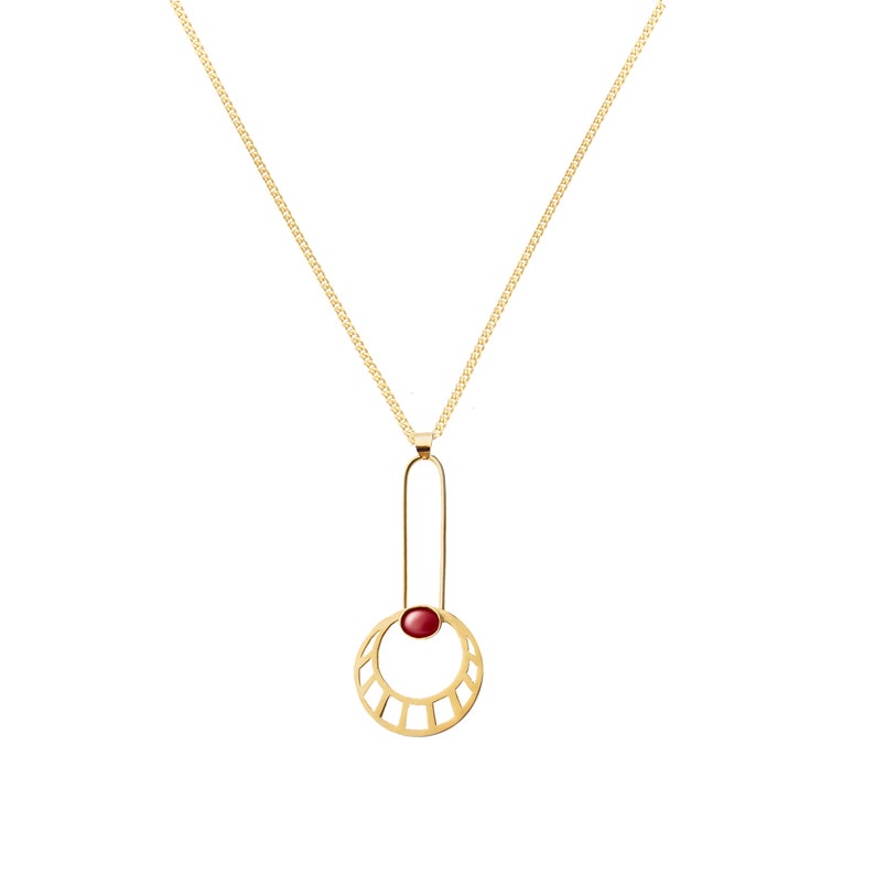 May include: A gold necklace with a pendant featuring a red gemstone set in a geometric circle design.
