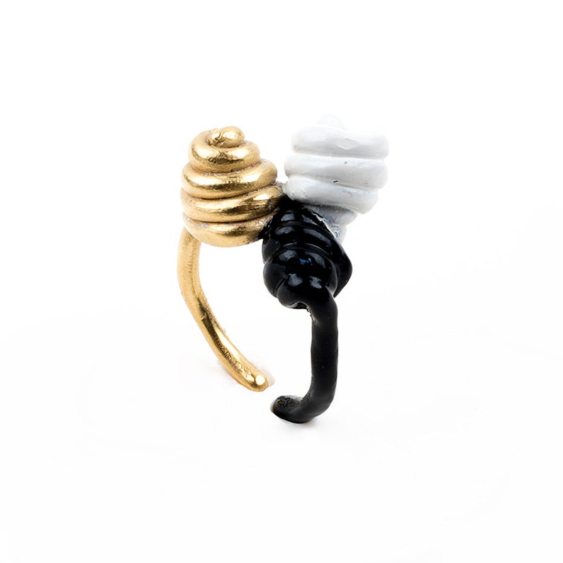 May include: A gold, white, and black ring with a unique twisted design. The ring is made of metal and has a smooth finish.