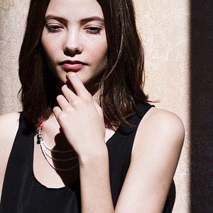 May include: A woman with long brown hair is wearing a black tank top and a silver bracelet with three round beads. She is wearing a layered necklace with a silver charm.