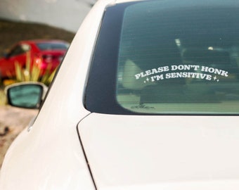 May include: A white car with a sticker on the rear window that reads "Please Don't Honk I'm Sensitive".