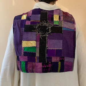 Könnte beinhalten: Eine violette Patchwork-Weste mit einem schwarzen Kreuz und einer goldenen Dornenkrone. Die Weste ist aus verschiedenen Stoffen gefertigt und hat eine gesteppte Textur.