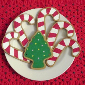 Puede incluir: Un plato blanco con cinco galletas de az&uacute;car con tem&aacute;tica navide&ntilde;a. Tres galletas tienen forma de bastones de caramelo con rayas rojas y blancas. Dos galletas tienen forma de &aacute;rboles de Navidad con glaseado verde y chispas blancas y amarillas.