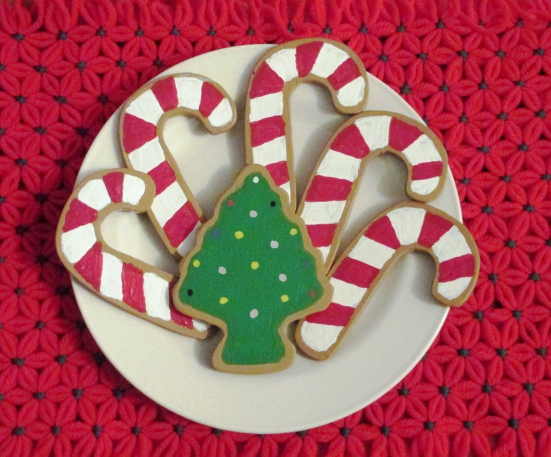 Puede incluir: Un plato blanco con cinco galletas de az&uacute;car con tem&aacute;tica navide&ntilde;a. Tres galletas tienen forma de bastones de caramelo con rayas rojas y blancas. Dos galletas tienen forma de &aacute;rboles de Navidad con glaseado verde y chispas blancas y amarillas.