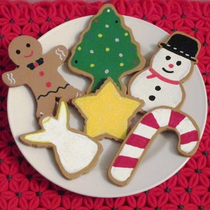 Puede incluir: Un conjunto de seis galletas de az&uacute;car con tem&aacute;tica navide&ntilde;a decoradas con glaseado. Las galletas tienen forma de hombre de jengibre, &aacute;rbol de Navidad, mu&ntilde;eco de nieve, bast&oacute;n de caramelo, estrella y &aacute;ngel. Las galletas est&aacute;n en un plato blanco.