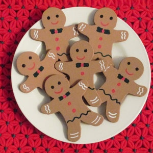 Puede incluir: Seis galletas de jengibre en forma de hombre en un plato blanco. Las galletas est&aacute;n decoradas con ojos de glaseado negro, sonrisas de glaseado rojo y corbatas de lazo de glaseado negro. El plato est&aacute; sobre una superficie de crochet roja y gris.