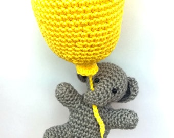 May include: A grey crocheted elephant holding a yellow crocheted balloon. The elephant has black eyes and a small mouth.
