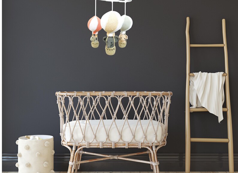 May include: A white wicker crib with a white mattress and a mobile hanging above it. The mobile has three crocheted hot air balloons with animal faces and a white base.