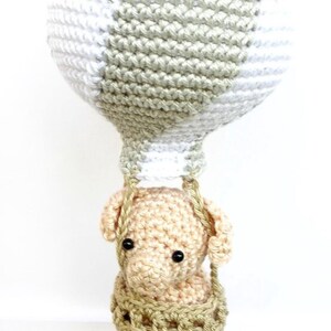 May include: A crocheted hot air balloon with a beige elephant in the basket. The balloon is white and green with a striped pattern.
