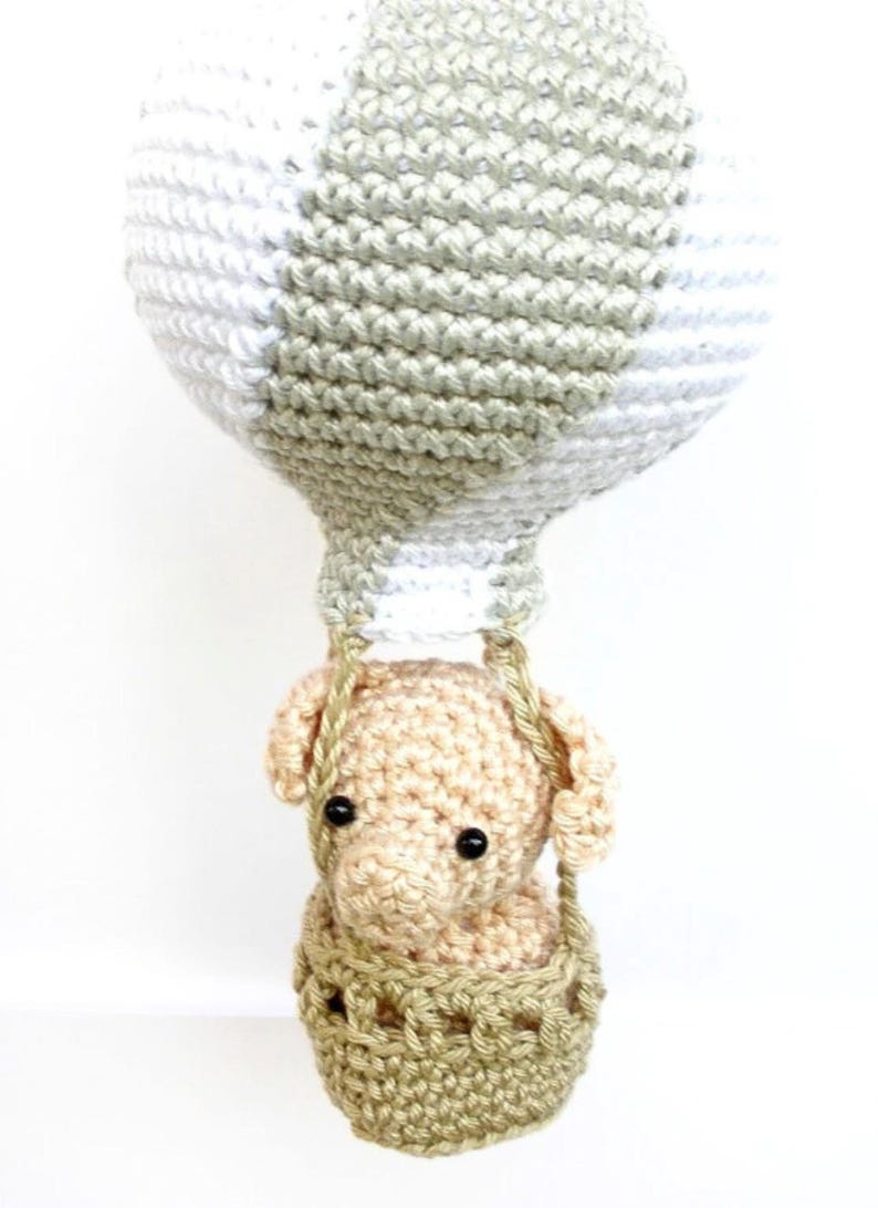 May include: A crocheted hot air balloon with a beige elephant in the basket. The balloon is white and green with a striped pattern.