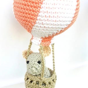 May include: A crocheted hot air balloon with a peach and white striped pattern. A small crocheted animal is sitting in the basket.