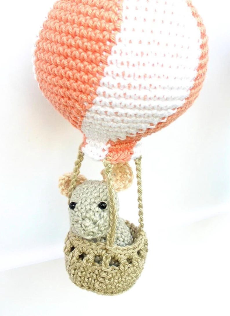 May include: A crocheted hot air balloon with a peach and white striped pattern. A small crocheted animal is sitting in the basket.