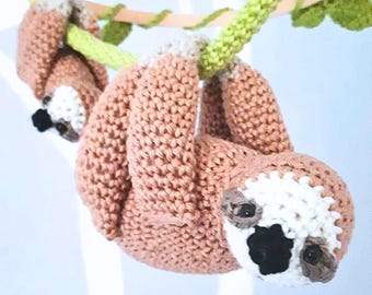 May include: Two crocheted sloth toys hanging from a green crocheted vine. The sloths are brown with white faces and black eyes.