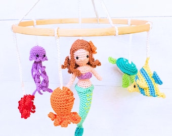 May include: A crocheted mobile featuring a mermaid, octopus, jellyfish, turtle, and a yellow fish. The mobile is made of wood and has a white background.